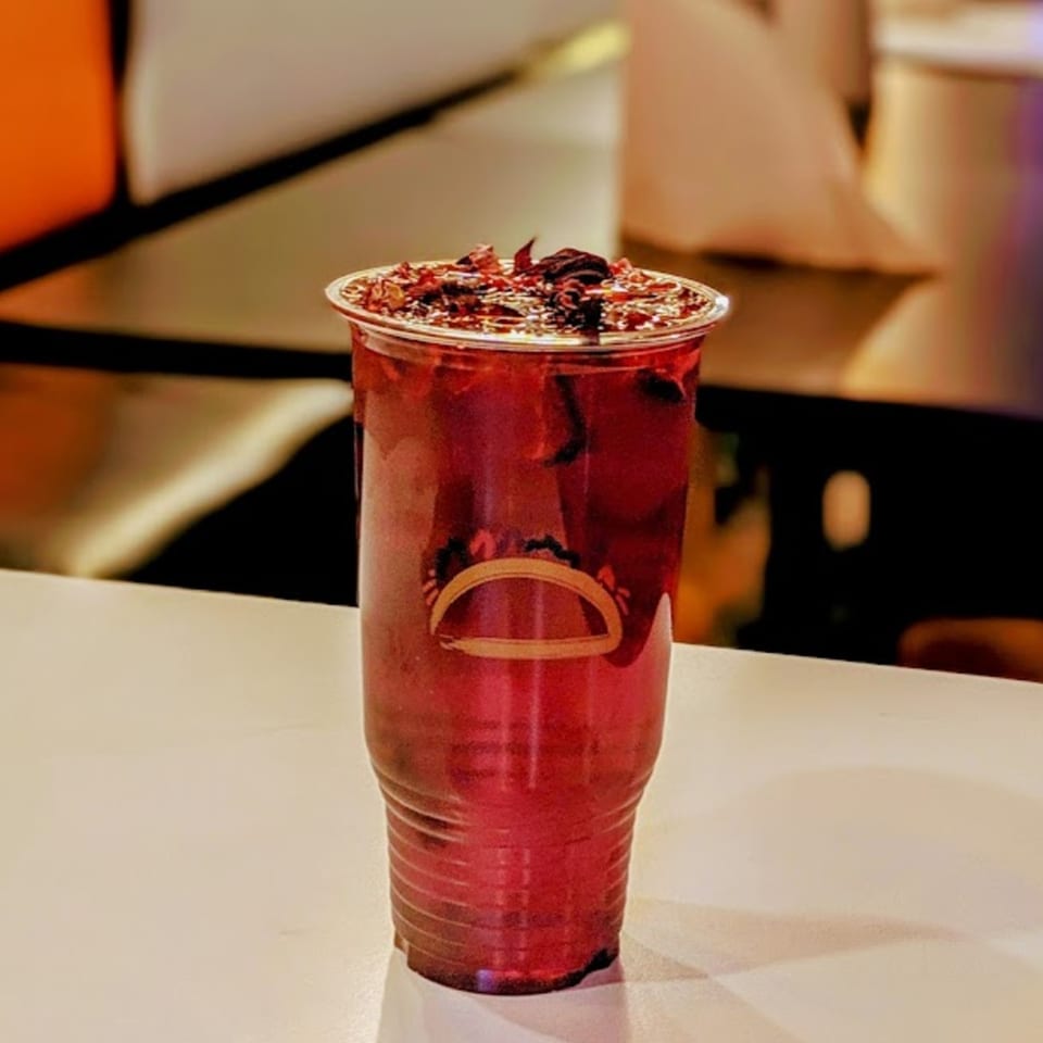A vibrant red hibiscus drink from Tacolandia, garnished with dried hibiscus petals, on a white counter.