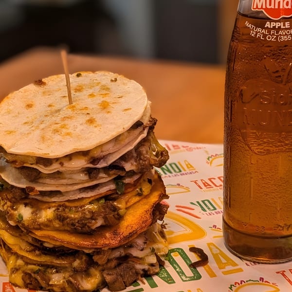 A tall stack of cheesy, meaty quesadillas from Tacolandia, next to an apple soda bottle.