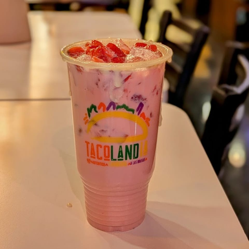 A pink strawberry drink with ice and fresh strawberries in a Tacolandia branded cup.