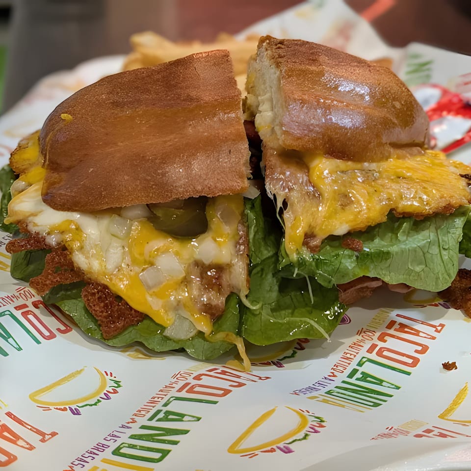 A Tacolandia Mexican torta sandwich, cut in half, with melted cheese, lettuce, and onions.