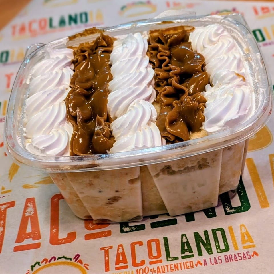 Tacolandia's tres leches cake with whipped cream and dulce de leche swirls in a clear container.
